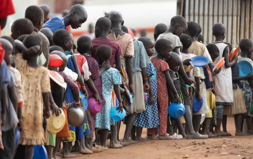 Children in Uganda wait in line with empty bowls for FMSC food.