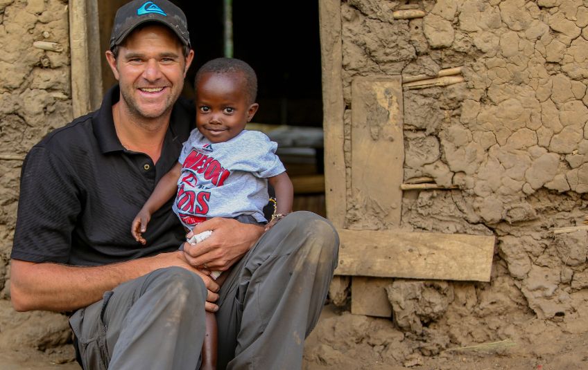 Man sitting with a child in front of a mud brick house