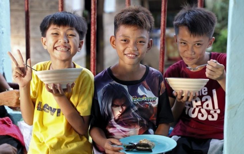 three boys smiling with bowls and plates of food